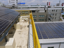 屋上の太陽光発電パネルは出力15kWで、2015 年度は年間電気使用量の約14%をまかなった発電力を持つ。ちなみに右下に見えるのは隣接するよその事業所の屋根だ。「うちが始めてから、まわりのビルが次々に太陽光発電パネルをつけ始めたんですよ」と古田さんが目を細める。温暖化防止への取組の伝播は、まさに社会貢献だろう