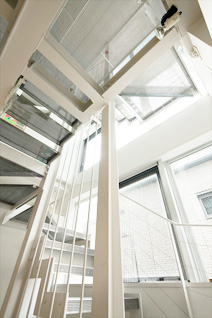 地階から最上階までを貫く階段室は、全面ガラス張りの壁やパンチングメタルの多用で自然光を取り込む「光の立体通り庭」。