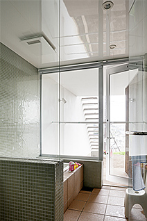 タイル張りの浴室は手前の洗面スペースともガラスで仕切られ、開放的。デッキから直接外に出ることができ、夫婦で精を出す庭づくりでかいた汗をそのまま流すにも好都合